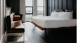 Une chambre d’hôtel moderne dotée d’un grand lit, d’un bureau avec une chaise et offrant une vue sur l’extérieur grâce à de grandes fenêtres.