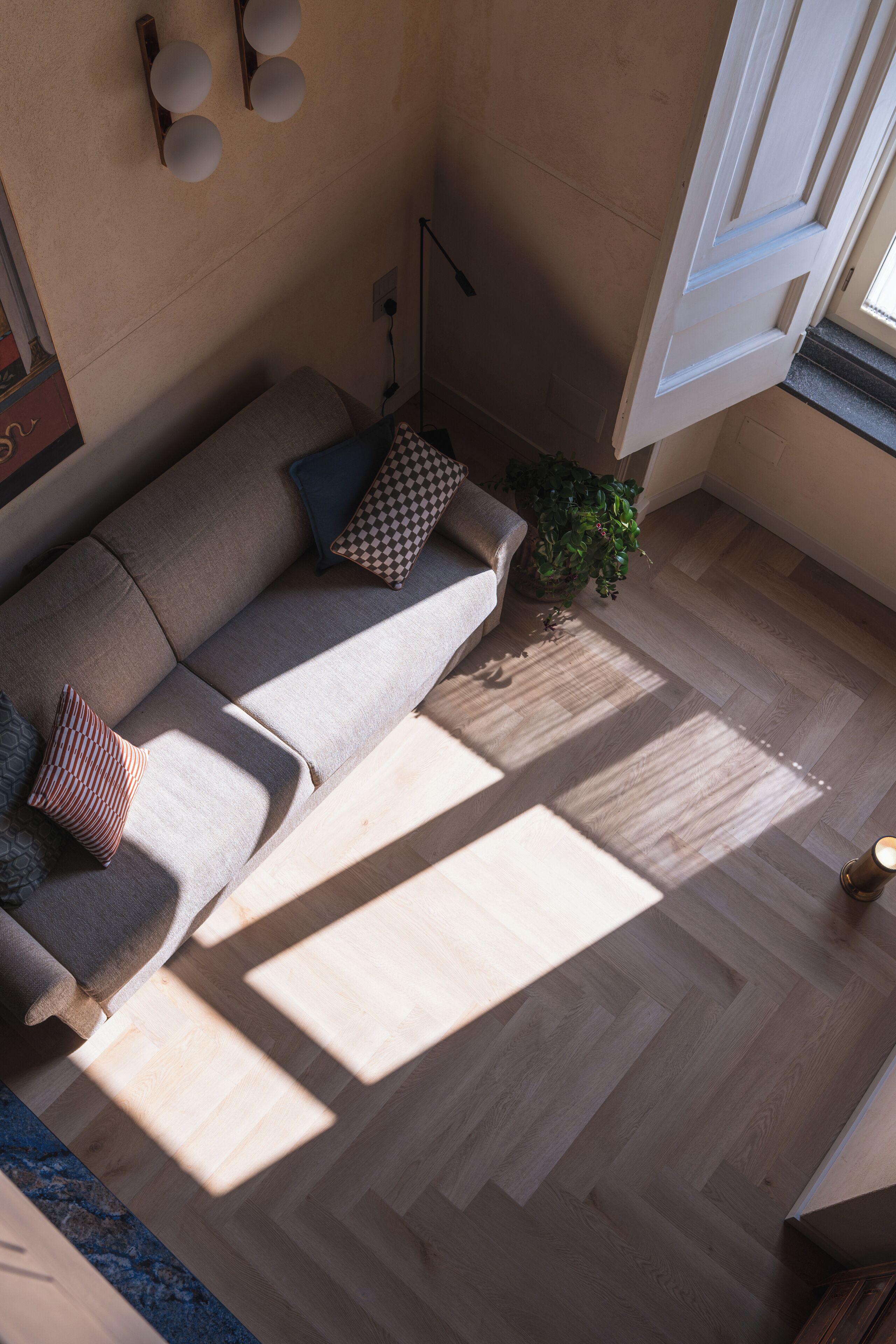 Un salon moderne avec un canapé, des coussins, une plante et un parquet à motifs en chevrons.