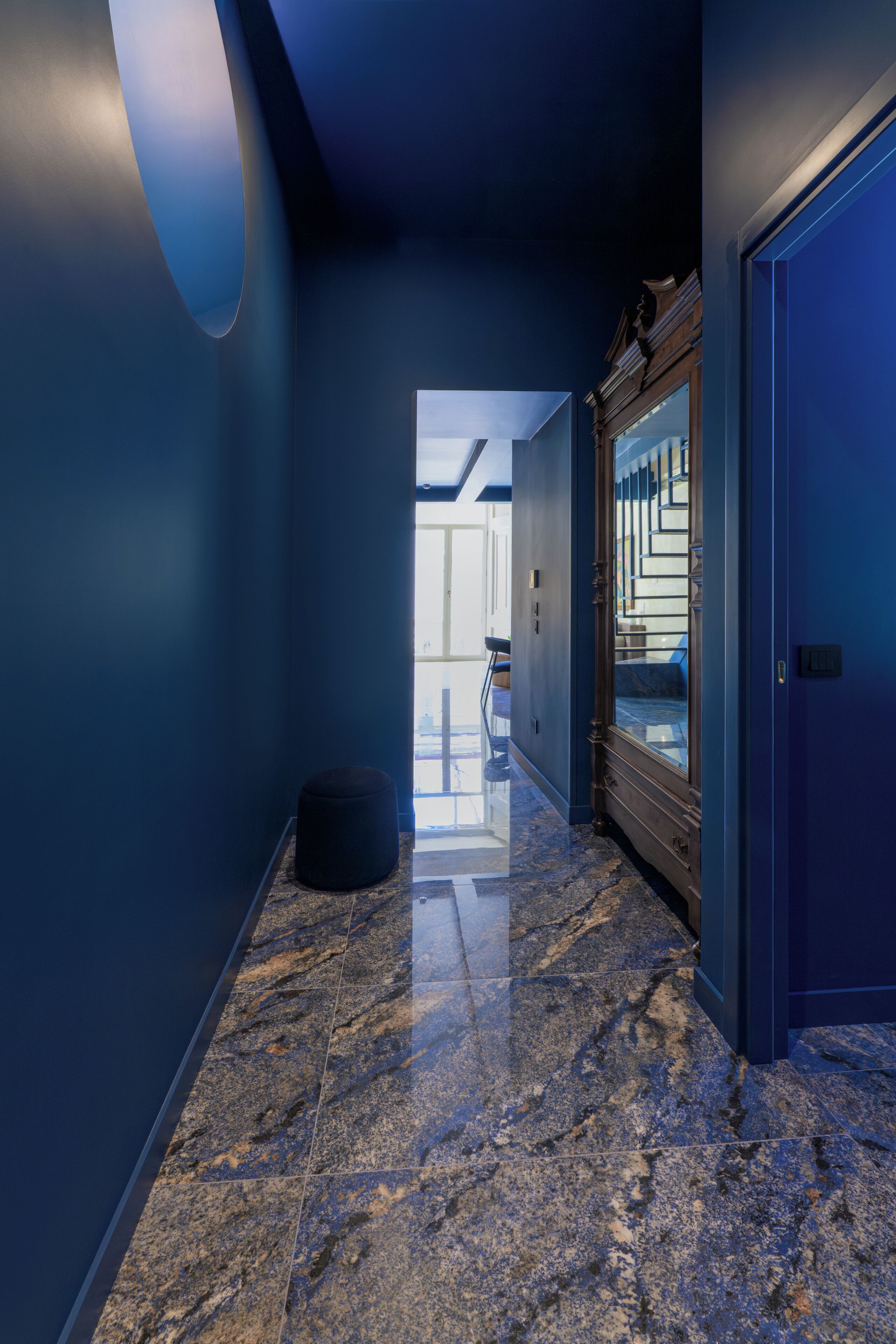 Un couloir aux murs bleu foncé, doté d’un sol en marbre et d’un grand miroir qui reflète un escalier.