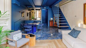 Amplia sala de estar con techo alto, escalera azul y cocina moderna.