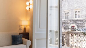 Una habitación de hotel moderna con sofá, un cojín estampado, una lámpara y vistas a un edificio de piedra a través de una puerta de cristal.