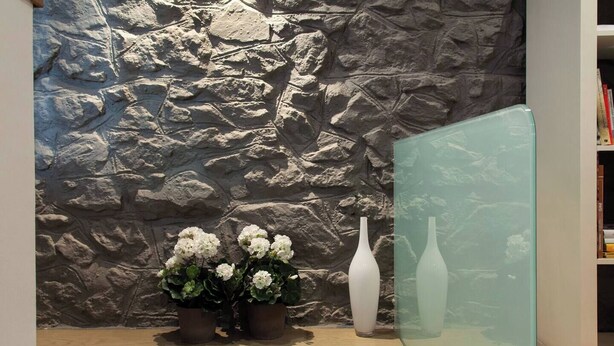 A stone wall, two potted plants with white flowers, and a tall white vase on a shelf.