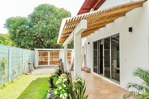 Una casa moderna con un porche cubierto, un patio trasero cercado y un árbol grande.
