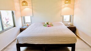 Ein ordentlich bezogenes Bett mit einer Steudecke, zwei Nachttischlampen und ein kleiner Tisch mit einem Blumenstrauß.