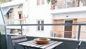 A balcony with a wooden table and two chairs, a bowl on the table, and a view of neighboring buildings.