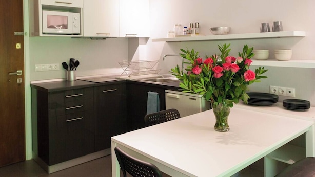 A modern kitchen with black cabinets, a white countertop, a microwave, a sink, and a vase with pink flowers.