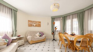 A room with a sofa, dining table, chairs, a lamp, and artwork on the wall. - Holiday Home 'Paraiso Para 4' with Shared Pool, Wi-Fi and Air Conditioning (Miami Platja)