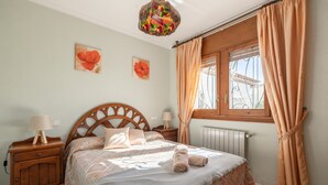 A bedroom with a wooden headboard, two bedside tables with lamps, a radiator, and a window with curtains. - Holiday Home 'Paraiso Para 4' with Shared Pool, Wi-Fi and Air Conditioning (Miami Platja)