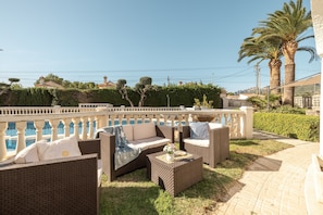 An outdoor seating area with wicker furniture, a small table with a flower vase, and a view of the sea.