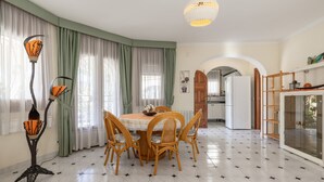A dining area with a round table, four chairs, a tall floor lamp, and a kitchen in the background. - Holiday Home 'Paraiso Para 4' with Shared Pool, Wi-Fi and Air Conditioning (Miami Platja)
