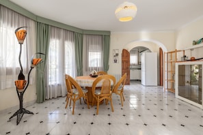 A dining area with a round table, four chairs, a tall floor lamp, and a kitchen in the background.