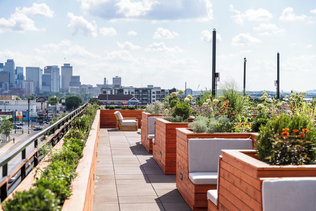 A rooftop terrace with seating and planters, overlooking a city skyline.
