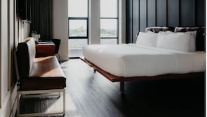Une chambre d’hôtel moderne dotée d’un grand lit, d’un bureau avec une chaise et offrant une vue sur l’extérieur grâce à de grandes fenêtres.