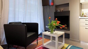 Una sala de estar moderna con un sofá de cuero negro, una mesita auxiliar blanca con un jarrón de tulipanes, un televisor de pantalla plana en la pared y una chimenea con repisa.