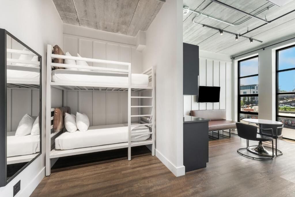 Ein modernes Hotelzimmer mit Stockbetten, einem Schreibtisch und einer Sitzecke mit Blick auf die Stadt.