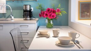 Una cucina moderna con un piano di lavoro bianco, una macchina da caffè e un vaso con fiori rosa.