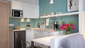Una cucina moderna con mobili bianchi, forno a microonde integrato, macchina del caffè e un vaso di fiori.