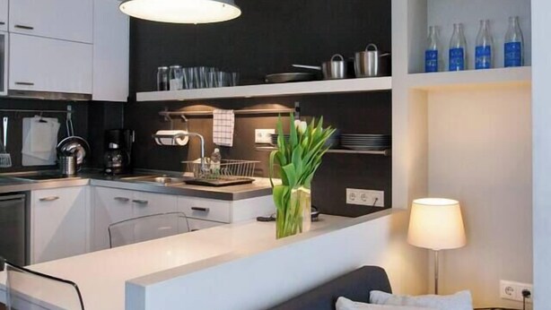 A modern kitchen with a central island, a dark-colored sofa with a cushion, and a pendant light above the island.