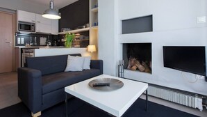 A modern living room with a sofa, a coffee table, a fireplace, and a kitchen area with cabinets and appliances.