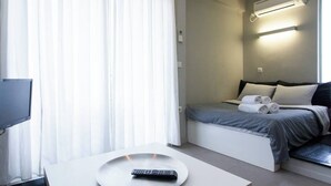 A modern hotel room with a bed, a TV, and a remote control on a table.