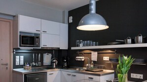 A modern kitchen with white cabinetry, a stainless steel microwave, a coffee machine, and a hanging pot rack.