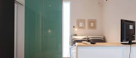 Une chambre avec un lit, un bureau avec un ordinateur, une télévision et une armoire verte.