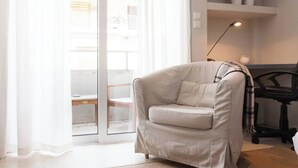 A modern living room with a beige armchair, a black office chair, a desk with a lamp, and a view through a glass door. - #AH34 Beige Studio (Athens)