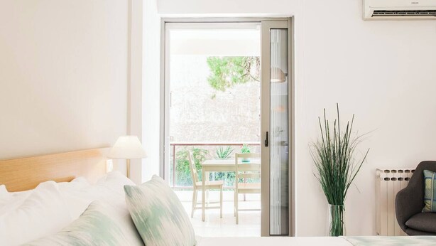 A hotel room with a bed, a nightstand, a lamp, a potted plant, and a view of an outdoor balcony with a table and chairs. - #FH10 New studio in Faliro (Paleo Faliro)