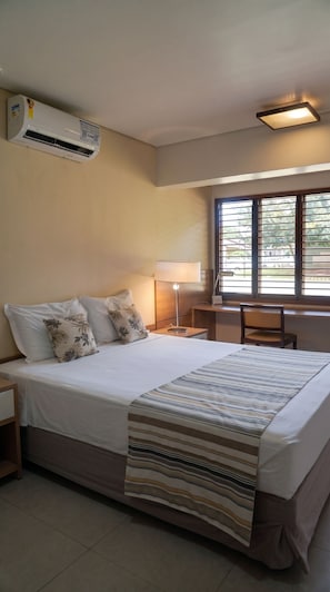 A hotel room with a bed, a desk, a lamp, and a window with blinds.