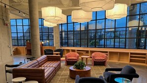 A spacious lounge area with a large sofa, armchairs, and a coffee table. There are multiple pendant lights and a large window providing a view outside.
