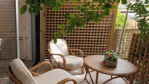 Un balcón con muebles de mimbre, incluyendo dos sillas y una mesita redonda, y un muro de celosía de madera.