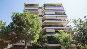 Un edificio de varios pisos con balcones, rodeado de árboles.