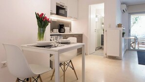 A modern kitchen with white cabinetry, a dining table with chairs, and a vase of red flowers. - #FH13 Garden level studio in Faliro (Paleo Faliro)