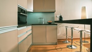 Eine moderne Küche mit hellen Schränken, einer schwarzen Arbeitsplatte und einem Edelstahlbackofen. Zwei Barhocker mit Metallbeinen sind vorhanden.