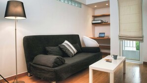 Ein modernes Wohnzimmer mit einem dunkelgrauen Sofa, einem weißen Couchtisch, einer Stehlampe und einem Fenster mit einer beigefarbenen Jalousie.
