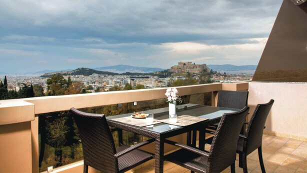 Ein Balkon mit Tisch und Stühlen, der Blick auf eine Stadtlandschaft mit einem markanten Hügel und einer Burg freigibt.
