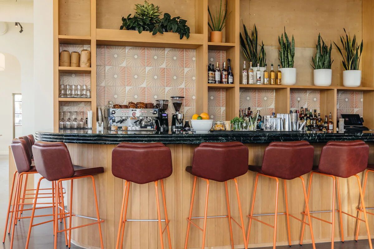 Zona de bar con estantes de madera, taburetes y una variedad de botellas y copas.