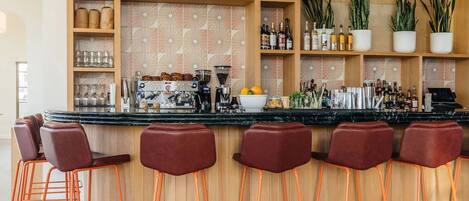 Zona de bar con estantes de madera, taburetes y una variedad de botellas y copas.