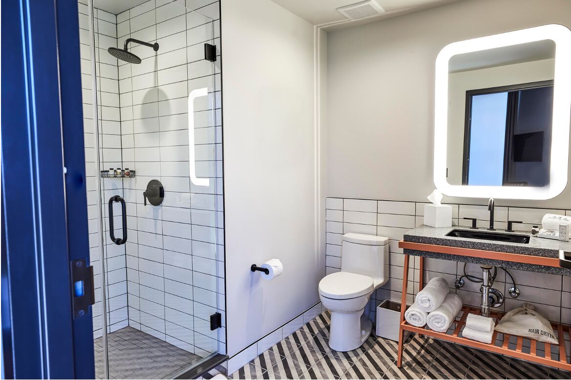 Une salle de bain moderne avec une douche à parois de verre, des toilettes blanches, un lavabo avec un miroir et un porte-serviettes.