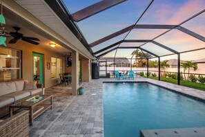 An indoor swimming pool with a glass ceiling, a sofa, and chairs on the patio.
