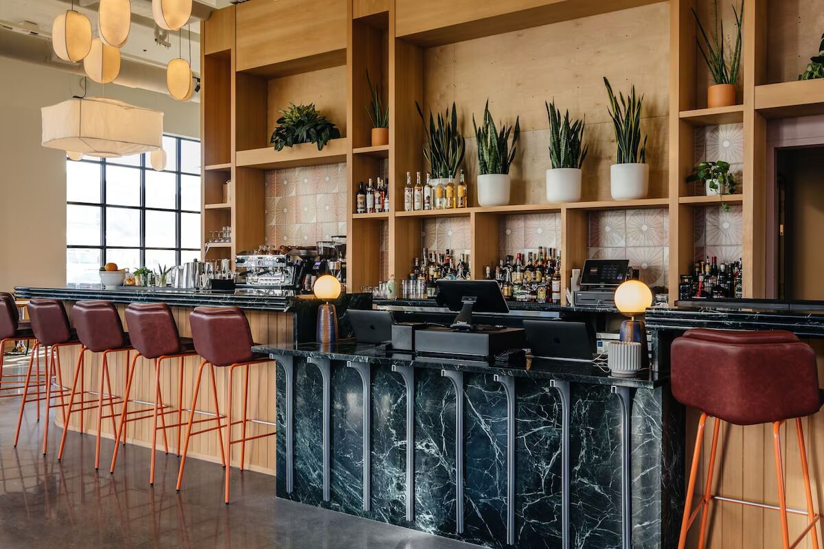 A bar area with a marble countertop, multiple stools, and shelves with plants and bottles.