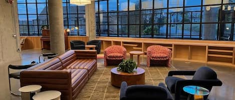 A spacious lounge area with a large sofa, armchairs, and a coffee table. There are multiple pendant lights and a large window providing a view outside.