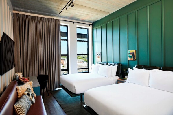 Une chambre d’hôtel avec deux lits, un téléviseur fixé au mur et une vue sur l’extérieur grâce à de grandes fenêtres.