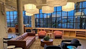 A spacious lounge area with a large sofa, armchairs, and a coffee table. There are multiple pendant lights and a large window providing a view outside.