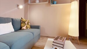 Una sala de estar con un sofá, una mesa de centro con libros y jarrones, estanterías con adornos y una lámpara de pie.