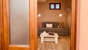 Una puerta de madera con un panel de vidrio esmerilado, una sala de estar con un sofá, una mesa de centro y una ventana pequeña.