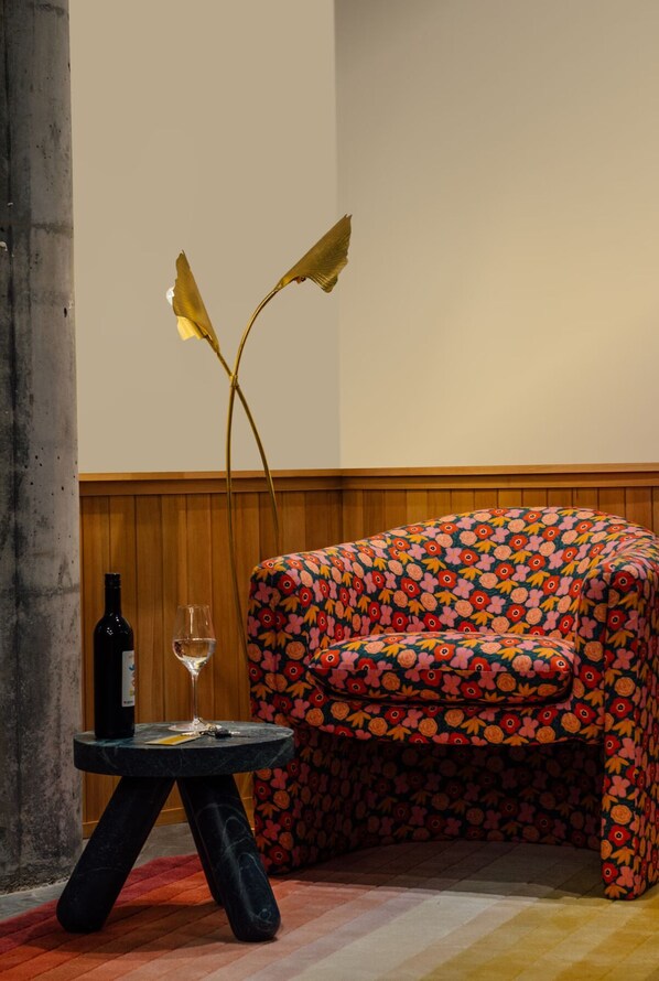 A room with a wooden panel wall, a black table with a wine bottle and glass, and a colorful floral sofa.