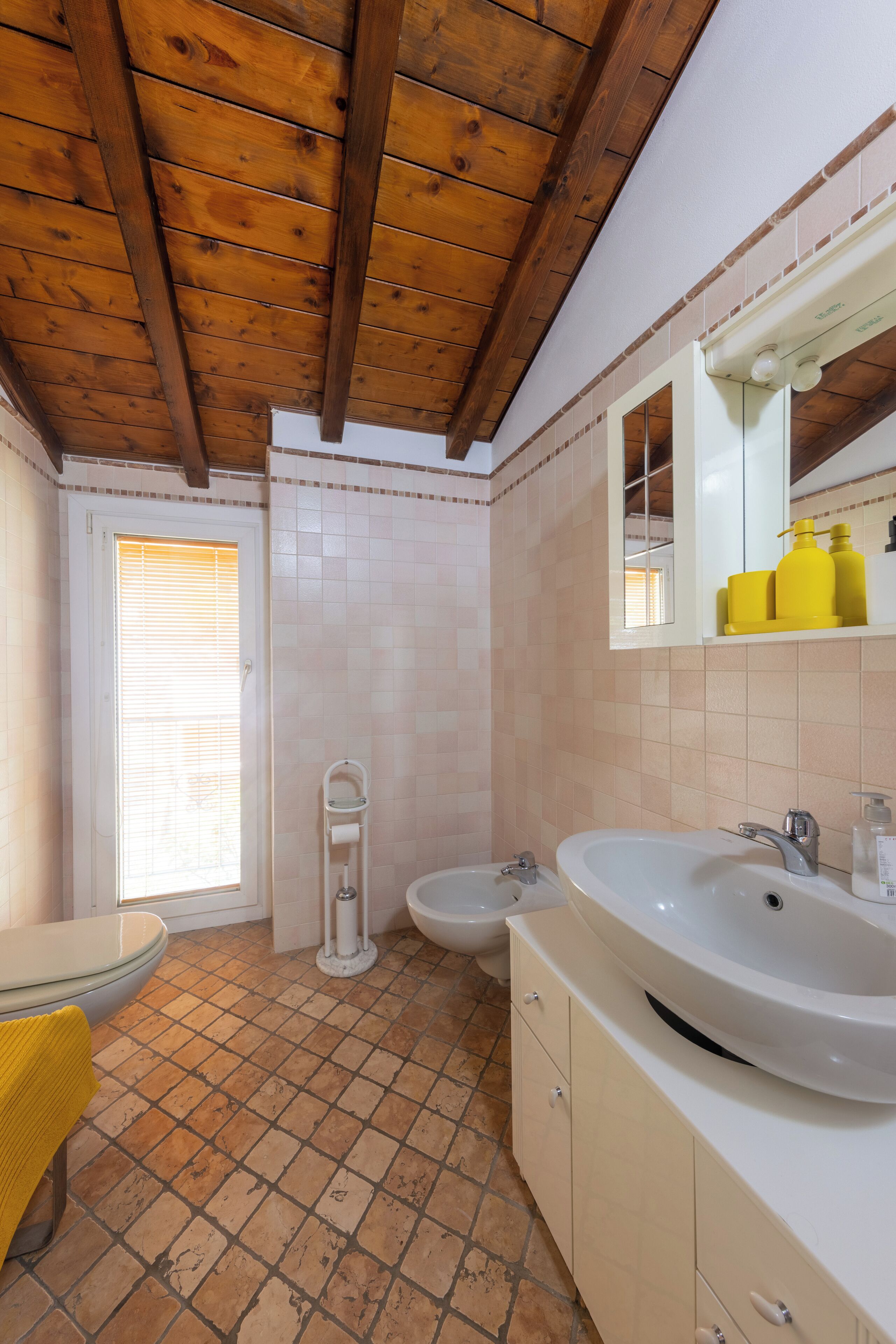 A bathroom with a wooden ceiling, a white sink, a bidet, and a yellow towel.