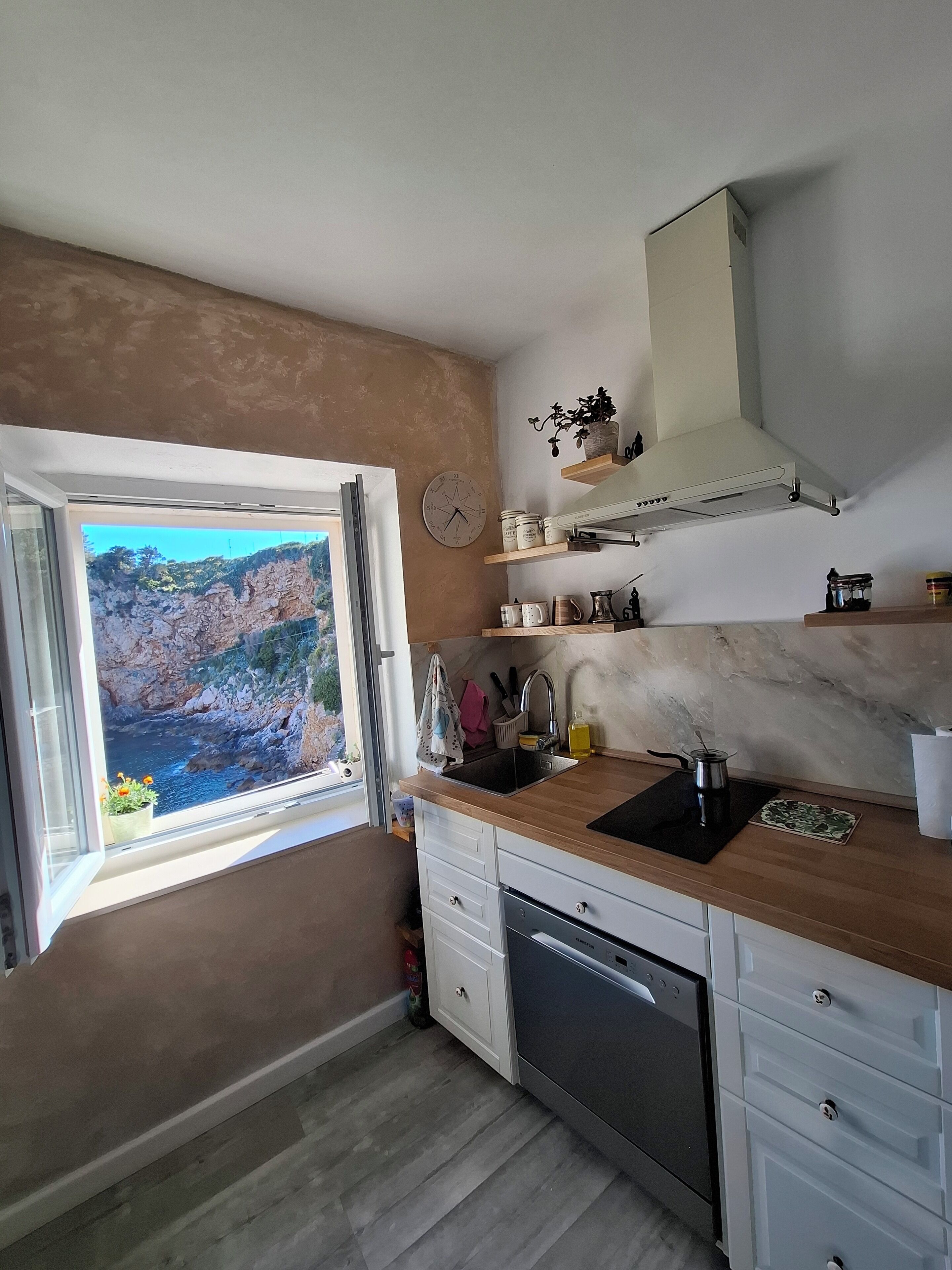 Eine Küche mit Blick auf eine felsige Landschaft durch ein Fenster, mit Holzarbeitsplatten, weißen Schränken und einem eingebauten Geschirrspüler.