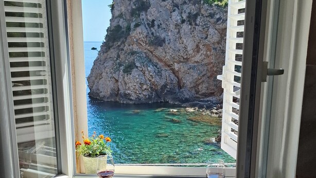 Habitación con vista a una costa rocosa y al mar. Hay dos copas de vino sobre un alféizar.